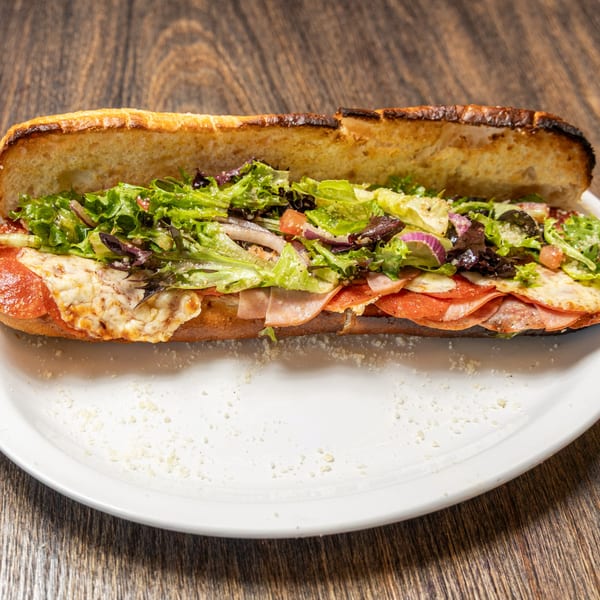 A toasted Italian sub sandwich with melted cheese, pepperoni, ham, and fresh green lettuce.