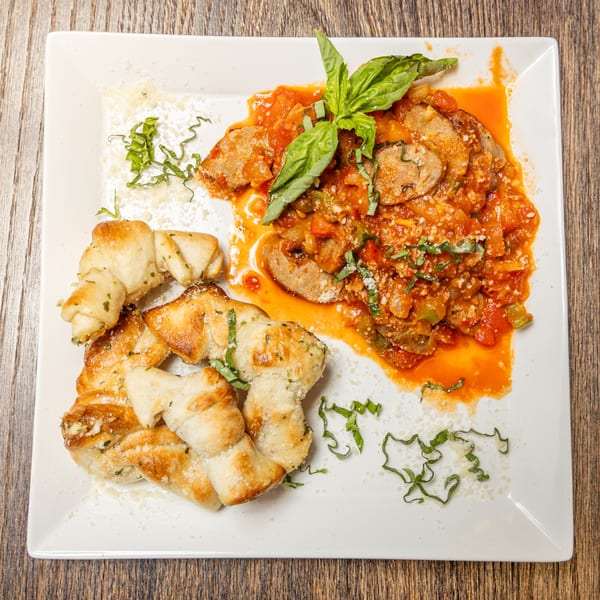 Sausage and peppers in red sauce with fresh basil and garlic knots on a white plate.