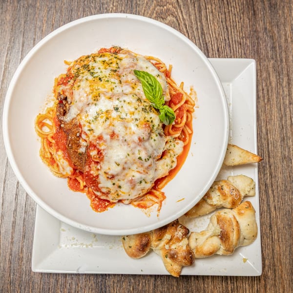 Chicken Parmesan with spaghetti, tomato sauce, melted cheese, basil, and garlic knots on a wooden table.
