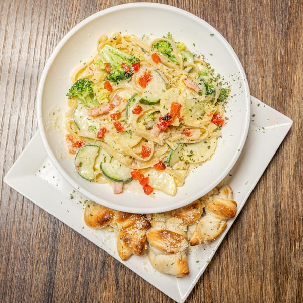 Creamy fettuccine pasta with broccoli, zucchini, and red peppers, served with garlic knots.